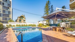Piscina com deck de madeira, espreguiçadeiras e área coberta com guarda-sol.