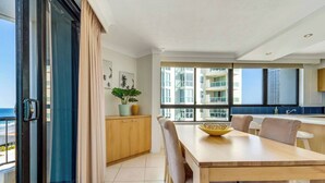 Uma sala de jantar moderna com uma mesa grande, cadeiras e vista para o mar através de grandes janelas.