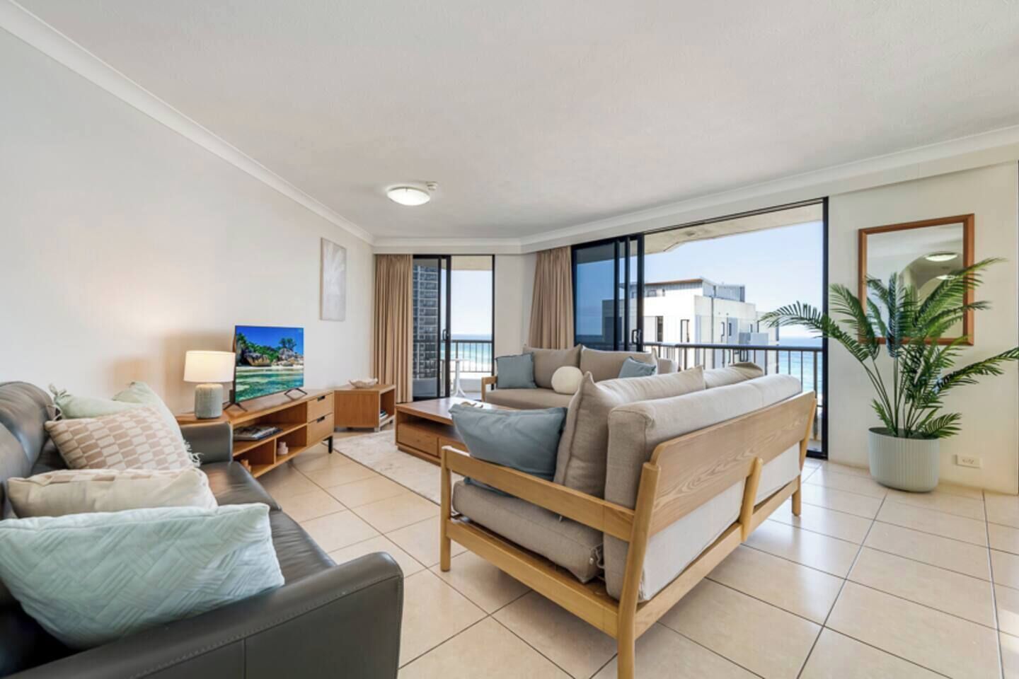 Un salon moderne avec un canapé, une table basse et un téléviseur. Il y a un balcon avec vue sur la mer.