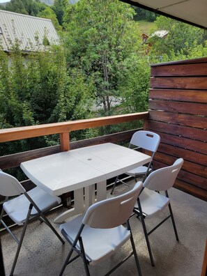 Ein Balkon mit einem weißen Tisch und vier Stühlen, der auf eine üppige, grüne Landschaft blickt.