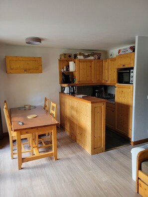 Eine kompakte Küche mit Holzausstattung, einer eingebauten Mikrowelle und einem Essbereich mit einem Holztisch und Stühlen.