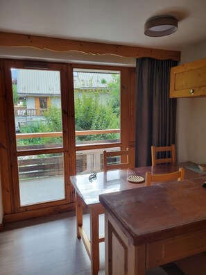 A wooden dining table with chairs, a view of greenery outside, and a sliding glass door. - QUIET APARTMENT FOR 6 PEOPLE, 45 m², South-Facing Balcony, Pool, Sauna, Steam Room (Valloire)