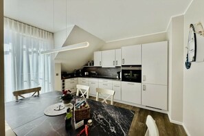 A modern kitchen with white cabinets, a black countertop, and a dining area with a marble table.