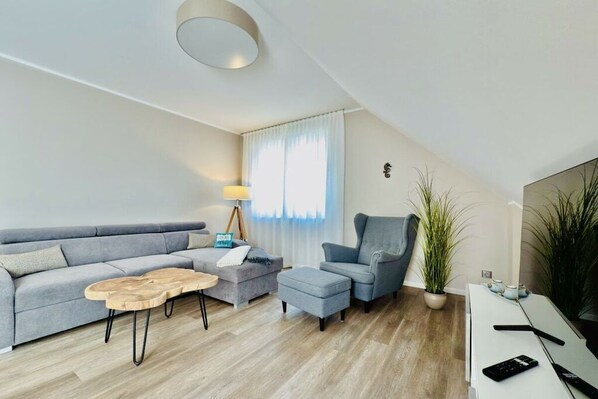 A modern living room with a grey sofa, a wooden coffee table, a grey armchair, and a white TV stand.