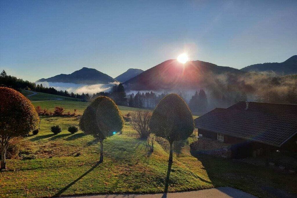 Un paysage rural avec une maison, des arbres et des montagnes en arrière-plan.