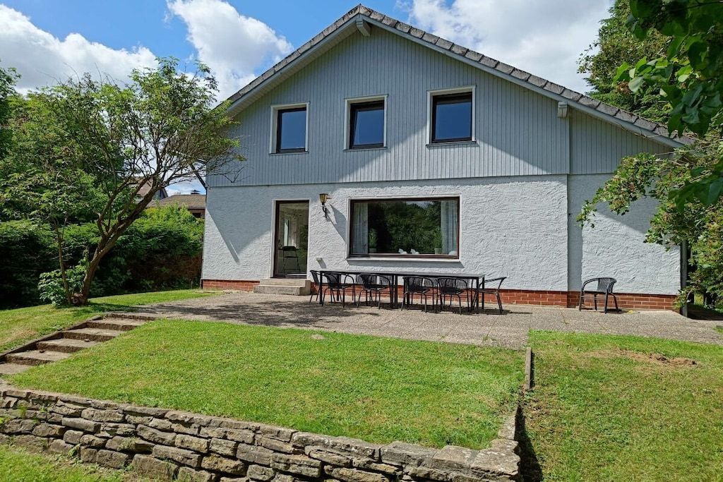 Et toetagers hus med en terrasse og en stenvæg i forgrunden.