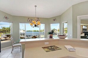 A kitchen with a large island, a chandelier, and large windows with a view of the outdoors. - CCVS - Villa Grandiosa (Cape Coral)