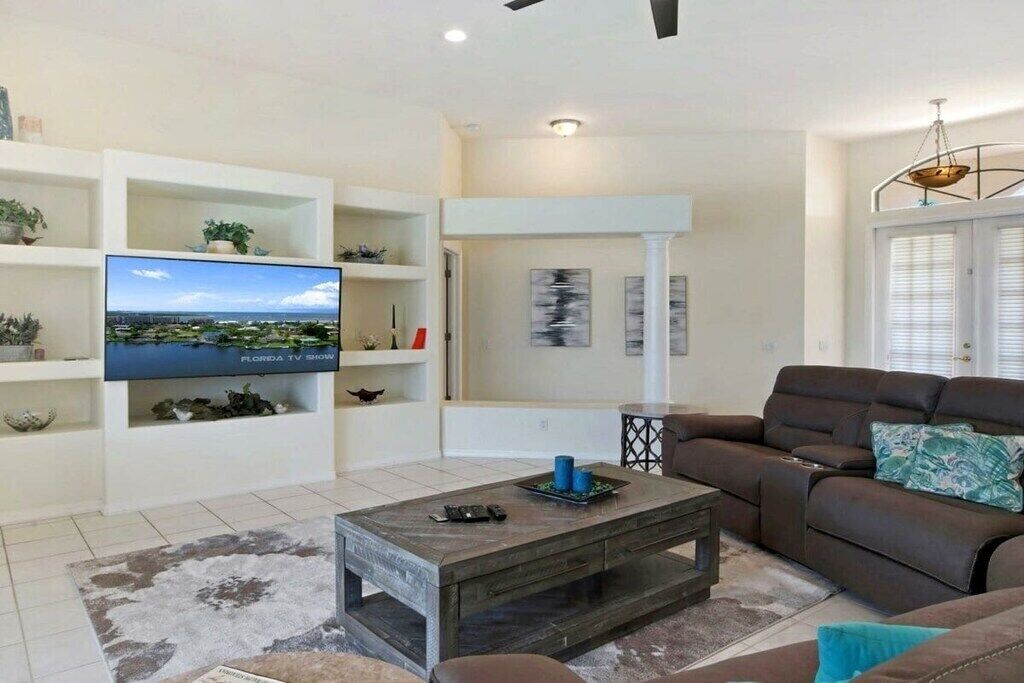 Ein Wohnzimmer mit einem Flachbildfernseher, einem braunen Ledersofa, einem Couchtisch und einer weißen Regaleinheit mit Dekoration.