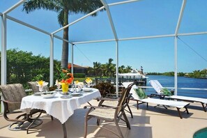 An outdoor dining area with a table set for two, overlooking a body of water and a boat. - CCVS - Villa Grandiosa (Cape Coral)