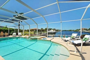 A pool area with a clear view of the water, surrounded by lounge chairs and a covered structure. - CCVS - Villa Grandiosa (Cape Coral)