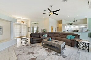 A spacious living room with a sectional sofa, a coffee table, and a ceiling fan. - CCVS - Villa Grandiosa (Cape Coral)