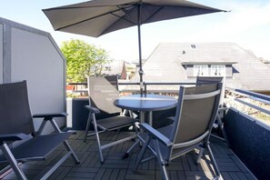 An outdoor deck with a table and chairs, a large umbrella, and a view of neighboring buildings. - Holiday apartment in Sylt with 2 bedrooms (Wenningstedt)