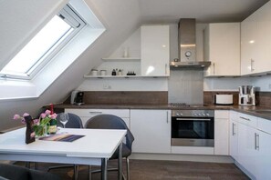 Ett modernt kök med vita köksskåp, en inbyggd ugn och en matplats med bord och stolar.