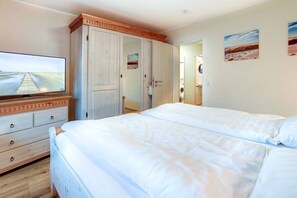 A hotel room with two beds, a television, a wardrobe, and a door leading to another room. - Sand Peter Apartment 1 (St. Peter-Ording)