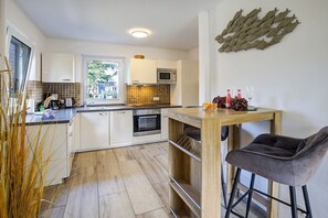 A compact kitchen with white cabinets, a microwave, and a wooden dining table with a bar stool. - Sand Peter Apartment 1 (St. Peter-Ording)