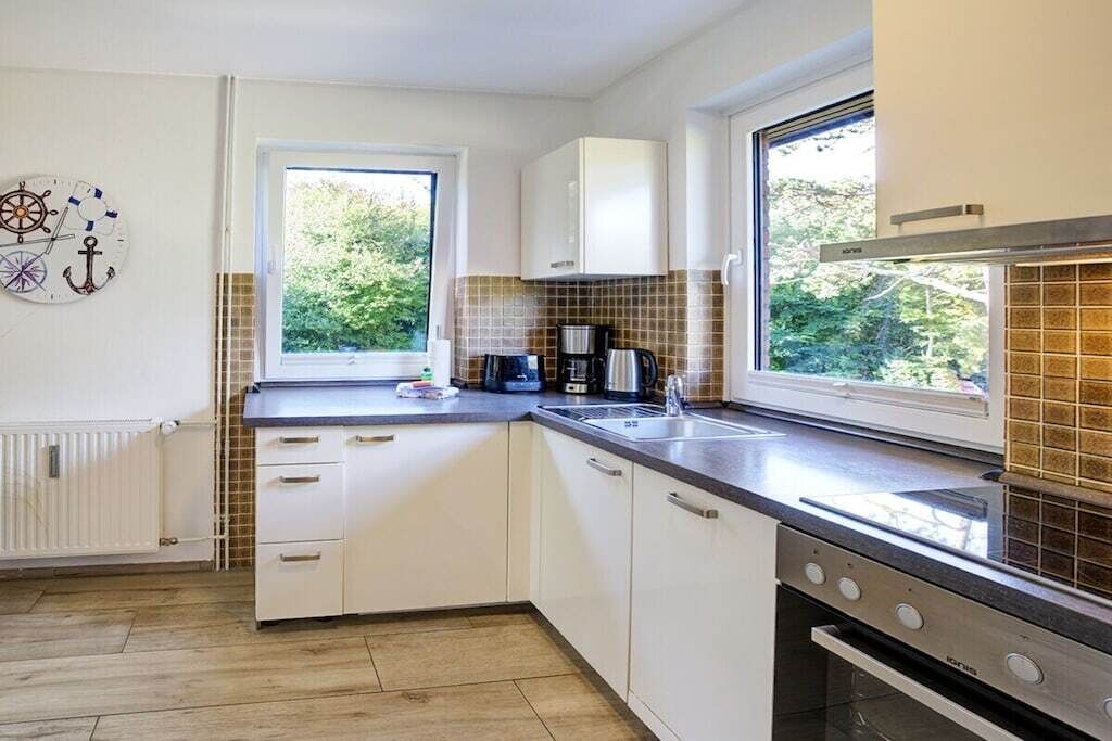 Una cocina moderna con armarios blancos, horno empotrado y ventana que proporciona luz natural.