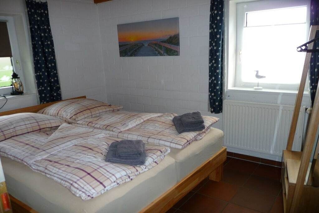 A room with two beds, a window with curtains, a radiator, and a painting on the wall.