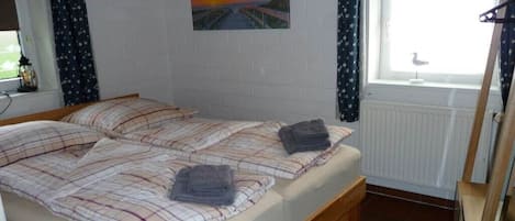 A room with two beds, a window with curtains, a radiator, and a painting on the wall.