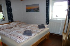 Una habitación con dos camas, una ventana con cortinas, un radiador y un cuadro en la pared.