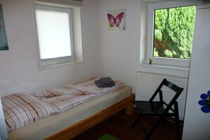 A small, single-bed room with a window, a chair, and a butterfly painting on the wall. - Holiday home with 1 bedroom (Otterndorf)