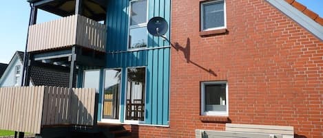 En tvåvåningsbyggnad med en balkong, en satellitparabol och en bänk utanför.