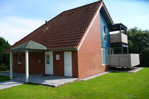 A two-story brick building with a sloped roof and a balcony on the upper floor. - Holiday home with 1 bedroom (Otterndorf)