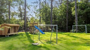 Une aire de jeux avec un toboggan et des balançoires, entourée d’arbres.
