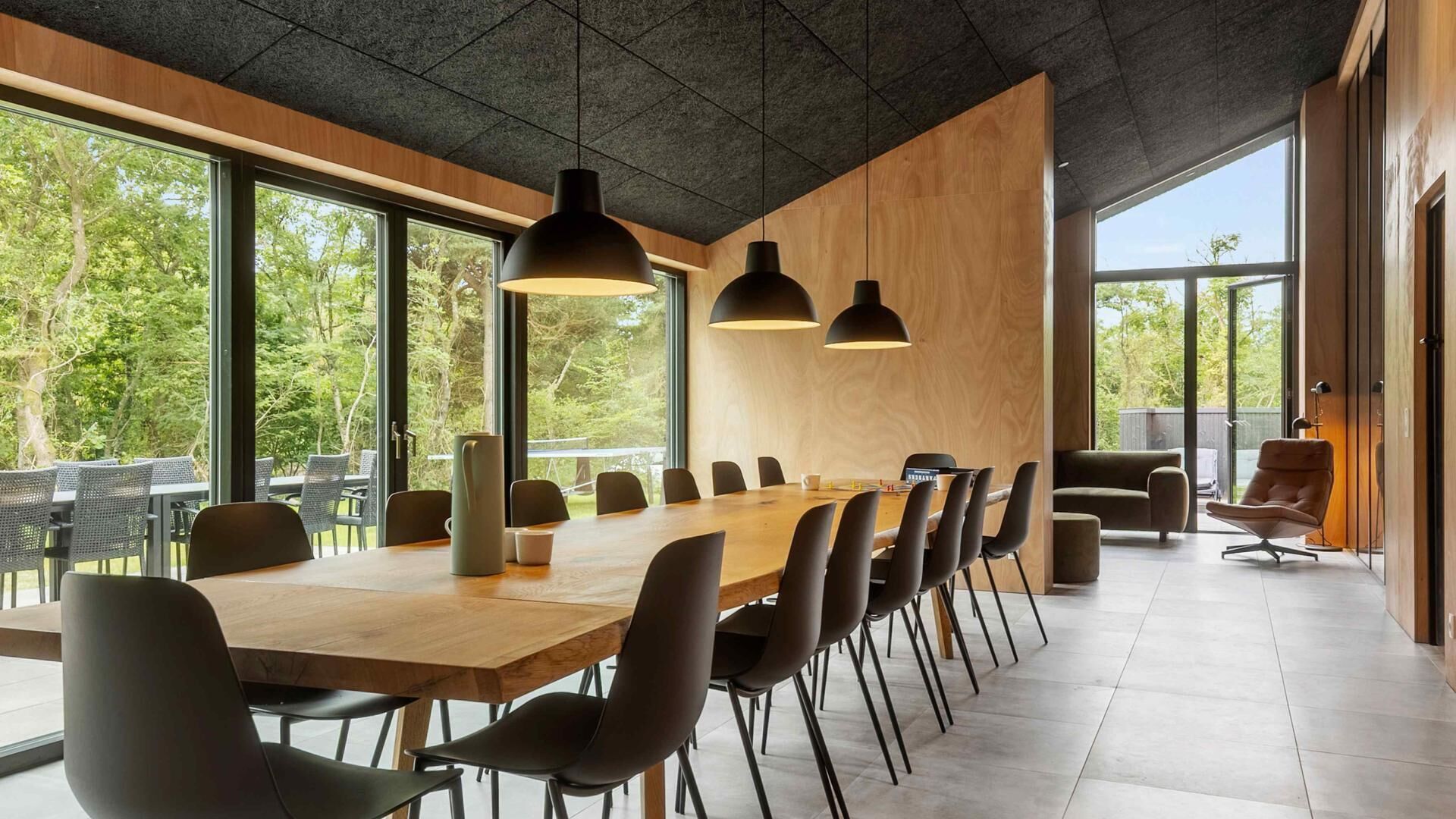 A modern conference room with a long wooden table, black chairs, and pendant lighting.