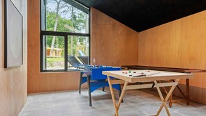 Une pièce équipée d’un baby-foot, d’une table de billard et d’une fenêtre donnant sur des arbres et un terrain de jeux.