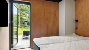 Une chambre avec un lit, un mur en bois et une porte-fenêtre coulissante donnant sur un espace extérieur.