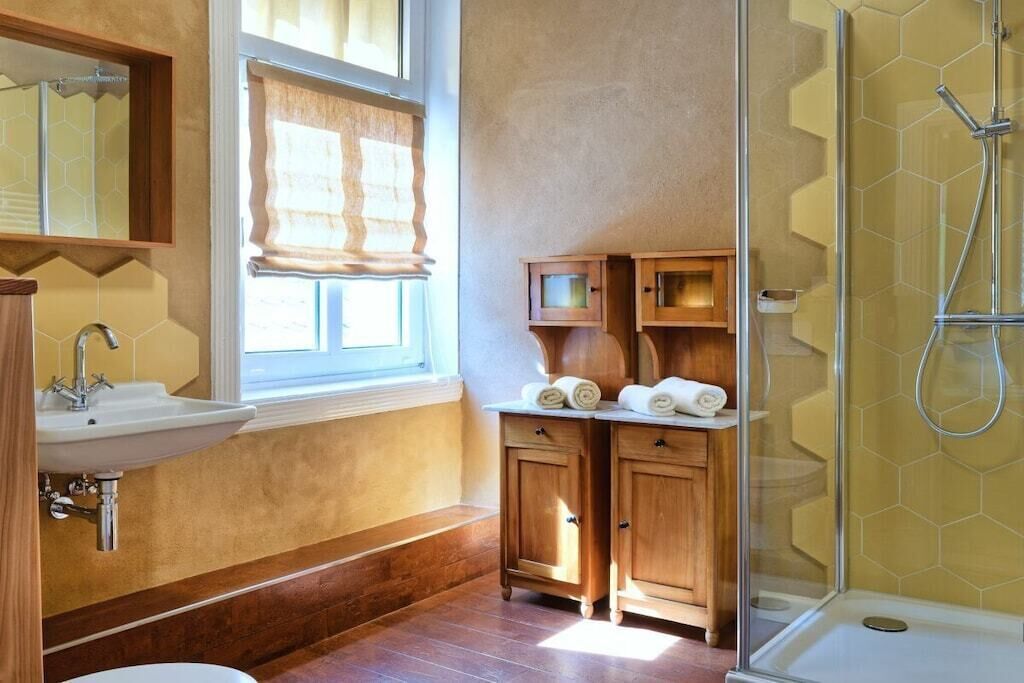 Ein Badezimmer mit einem Holzkosmetikschrank, einem Waschbecken, einer Dusche mit Glasabtrennung und einem Fenster mit Jalousien.