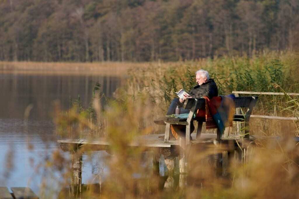 Iemand zit op een houten steiger boven het water, met een bos op de achtergrond.