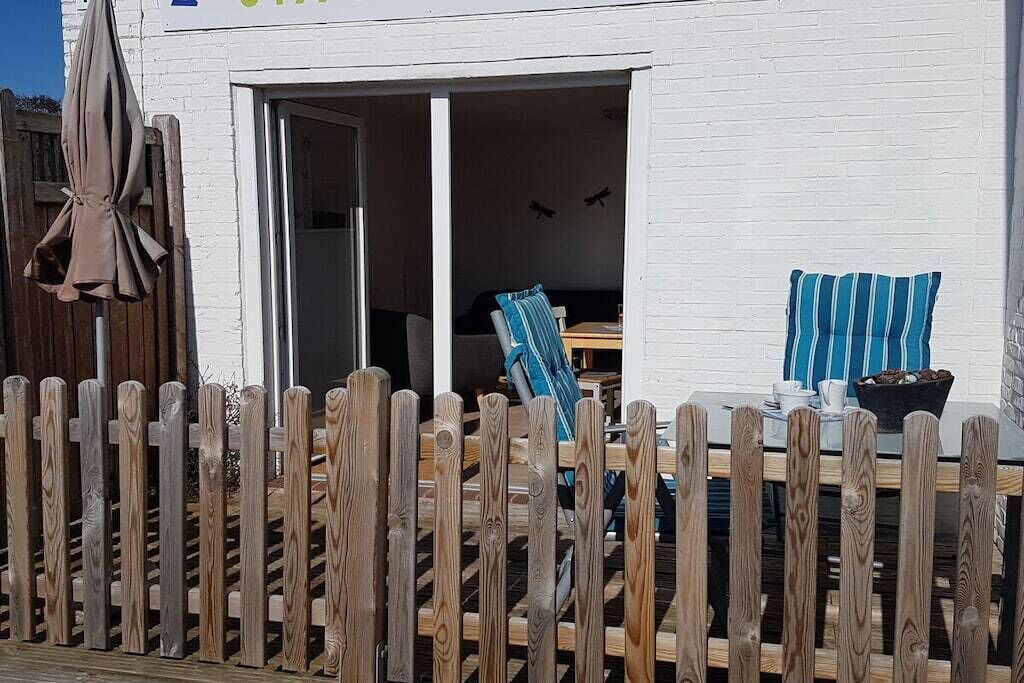 Un bâtiment blanc avec une clôture en bois, une table avec des chaises et un coussin à rayures bleues.