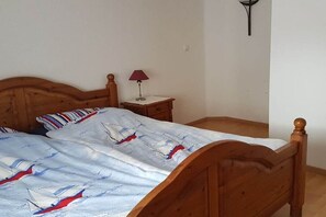 Een houten bed met een sprei met zeilbootmotief, een nachtkastje met een lamp en een wandlamp.