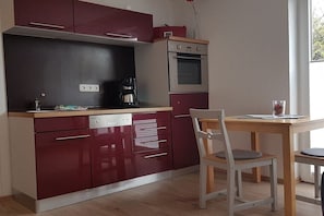 Una cocina compacta con lavavajillas, cafetera y horno doble. Hay una mesa de comedor con una silla.