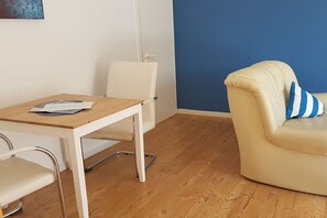 Une pièce avec une table en bois, des chaises blanches, un mur bleu et un canapé de couleur crème agrémenté d’un coussin à rayures.