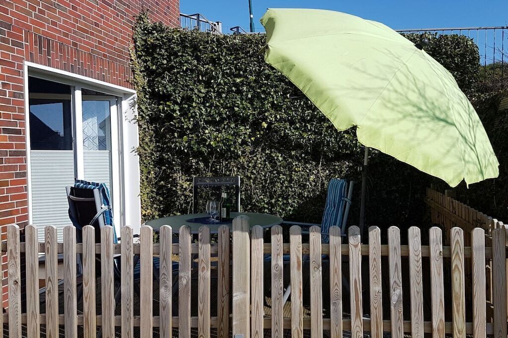 A brick building with a wooden fence, a table with chairs, and a green umbrella.