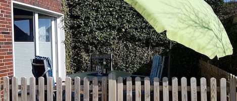 Un edificio de ladrillo con una valla de madera, una mesa con sillas y un paraguas verde.