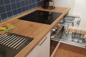 A kitchen with a black induction cooktop, a coffee maker, and a dishwasher. - Holiday apartment with 1 bedroom (Dornumersiel)