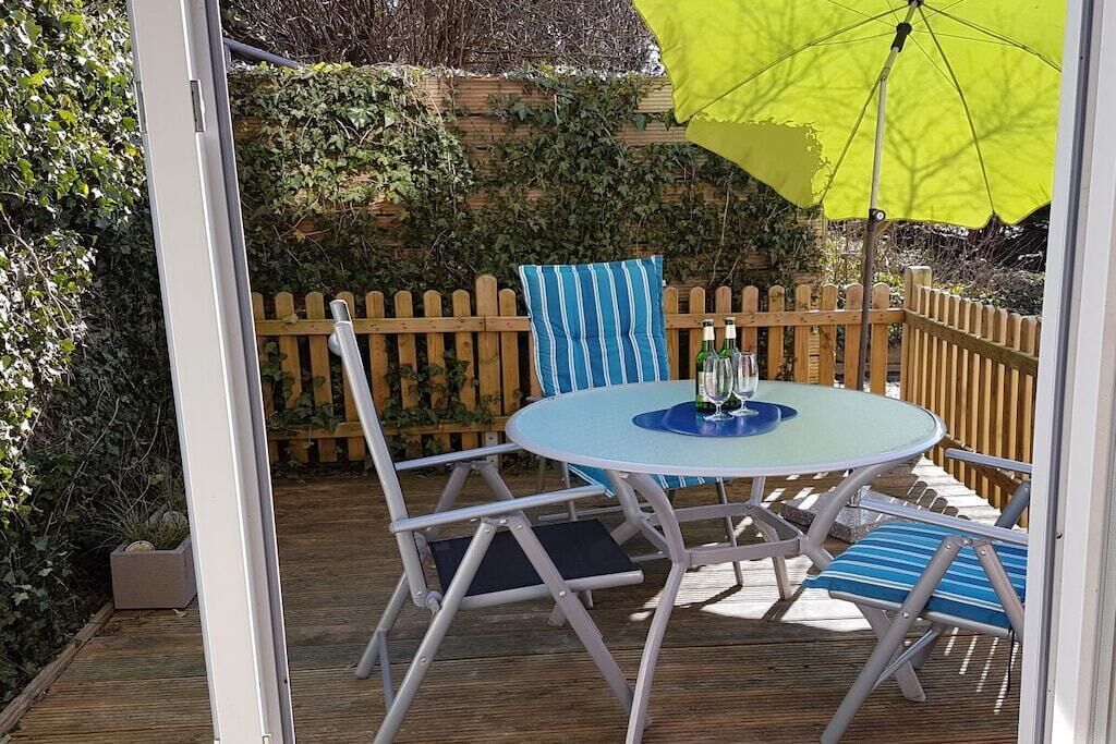 Eine Terrasse im Freien mit einem runden Tisch und Stühlen, einem gelben Sonnenschirm und einem Holzzaun.