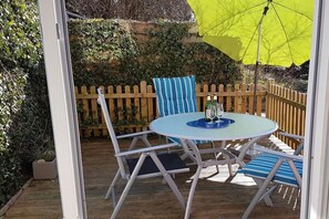 Une terrasse extérieure avec une table ronde et des chaises, un parasol jaune et une clôture en bois.
