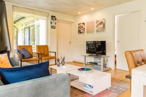 Ein modernes Wohnzimmer mit einer Couch, Sesseln, einem Couchtisch, einem Fernseher und Kunstwerken an den Wänden.