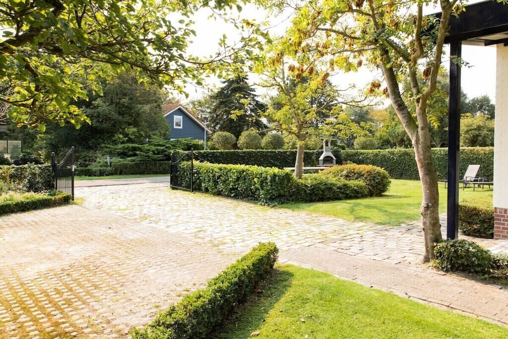 Ein gepflasterter Weg führt zu einem Haus mit einem gepflegten Garten, einer Hecke und einem Backsteinbau.