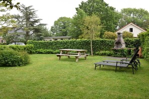 Ein Garten mit Picknicktisch, Liegestühlen und einem Grill.