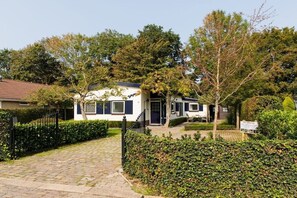 Een gelijkvloers huis met een geplaveid pad, een zwart metalen hek en een verzorgde haag.