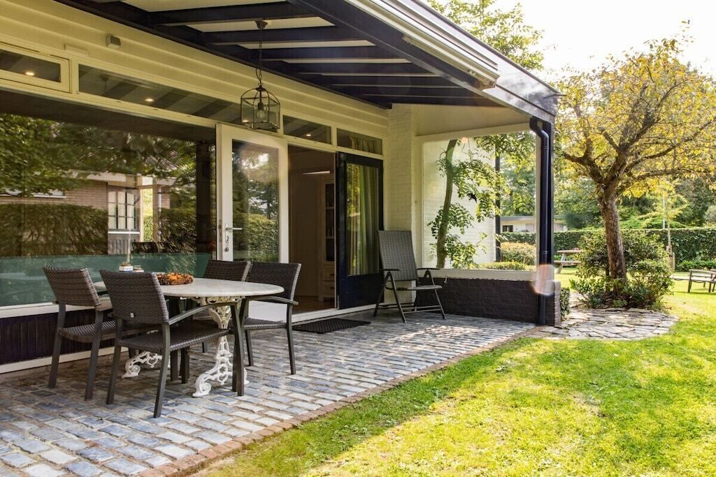 Une terrasse extérieure avec un sol en briques, une table entourée de chaises et un espace abrité doté d’un plafond.