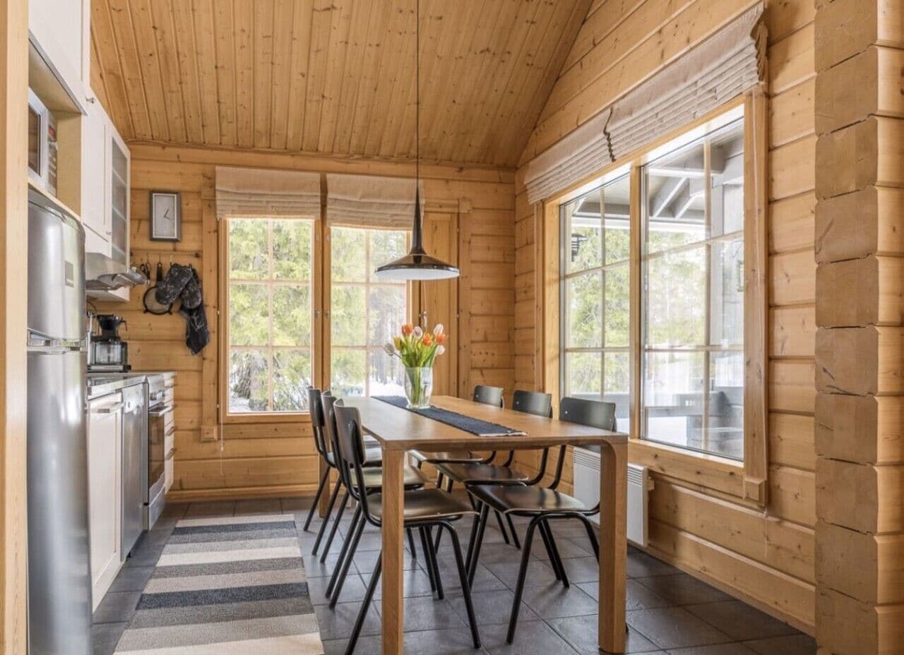 Un intérieur en bois comprenant une table à manger, des chaises, un coin cuisine et de grandes fenêtres.