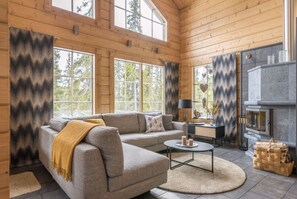 A log cabin interior with a sofa, coffee table, fireplace, and large windows. - Ihtinginrinne | Peaceful 2BR Log Villa by the Lake (Ruka)