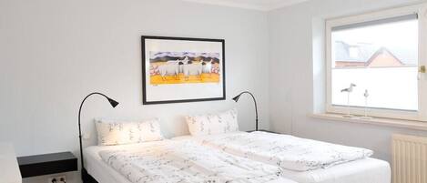A bedroom with a bed, a window, and a wall-mounted picture.