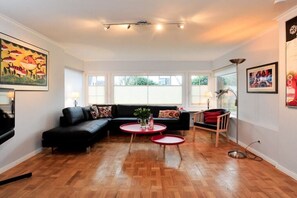 A living room with a black sofa, two red round tables, and a wooden floor. - Grutte Budde in the house Dünenblick (Westerland)